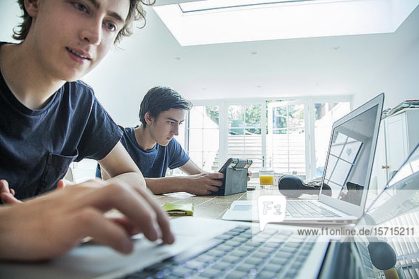 Zwei Jungen im Teenager-Alter benutzen zu Hause Laptop und Tablett auf dem Tisch