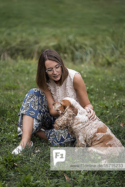 Frau sitzt mit ihrem Hund auf einer Wiese