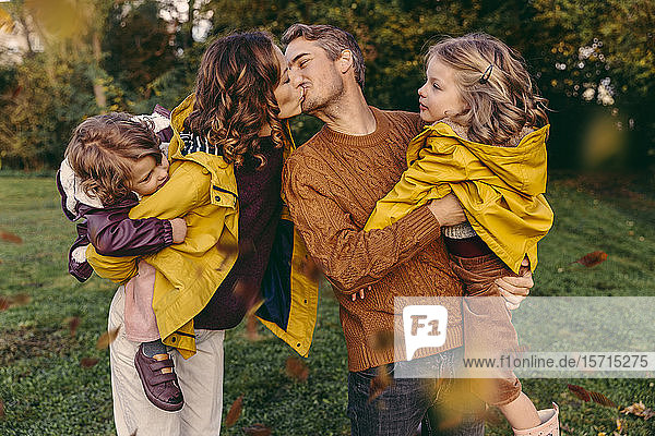 Couple kissing outdoors in autumn watched by her daughters