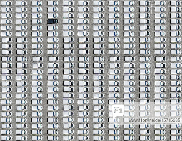 Aerial view of single black car parked between exclusively white ones