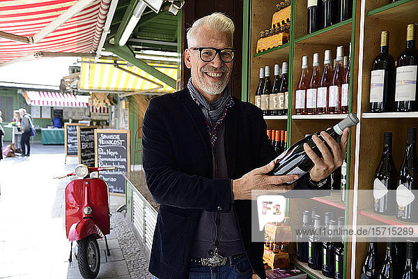 Portrait of smiling mature man choosing bottle of wine at a wine shop