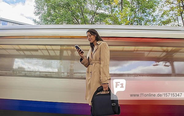 Junge Geschäftsfrau benutzt Smartphone vor dem Pendlerzug