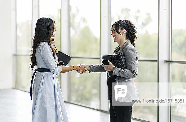 Two happy businesswomen shaking hands at the window
