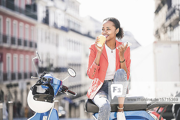 Lächelnde junge Frau mit Motorroller beim Kaffeetrinken in der Stadt  Lissabon  Portugal