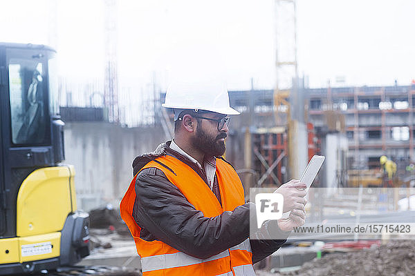Construction engineer wearing hard hat and safety vest usimng tablet at construction site
