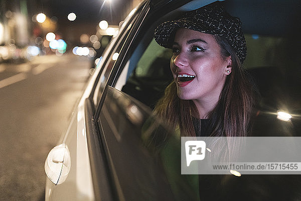 Frau  die nachts auf dem Rücksitz eines Autos in der Stadt sitzt und aus dem Autofenster schaut
