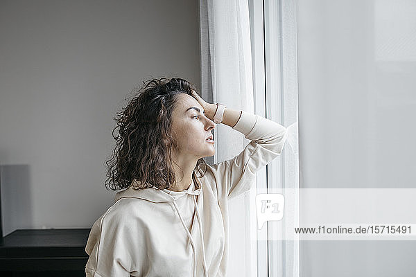 Porträt einer nachdenklichen Frau  die aus dem Fenster schaut