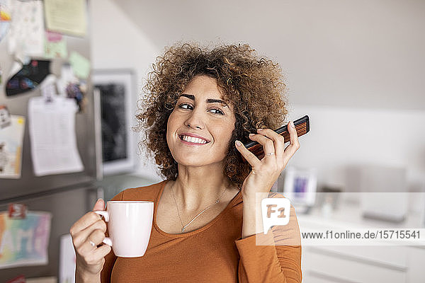 Frau hält Mobiltelefon und Kaffeetasse zu Hause