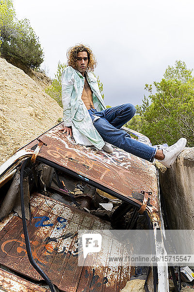 Young blond man sitting on junk car