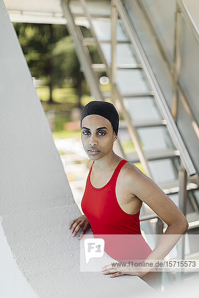Portrait of young woman wearing swimming cap and red bathsuit standing on stairs of highboard