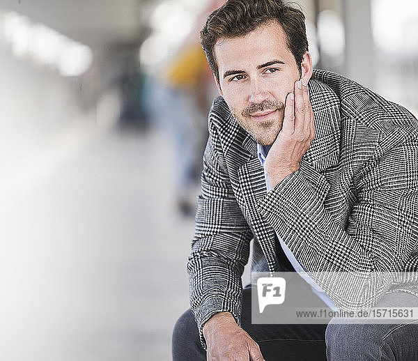 Porträt eines jungen Geschäftsmannes  der am Bahnhof sitzt