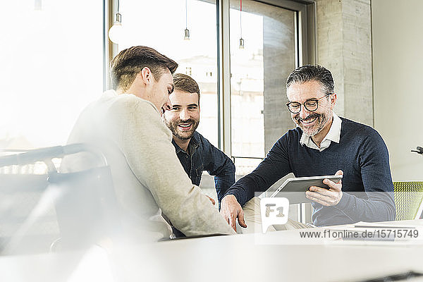 Drei glückliche Geschäftsleute bei einer Besprechung im Büro  die sich ein Tablett teilen
