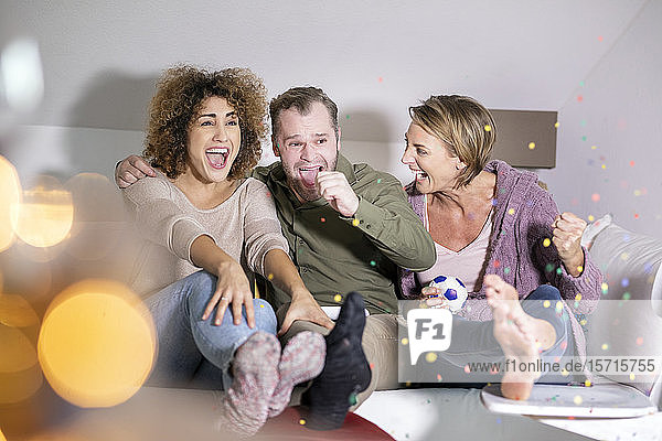 Drei Freunde sitzen auf dem Sofa und sehen sich ein Fußballspiel im Fernsehen an