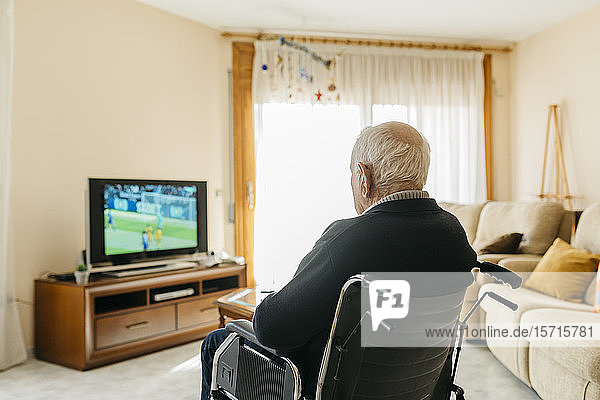 Back view of senior man sitting in wheelchair watching TV at home