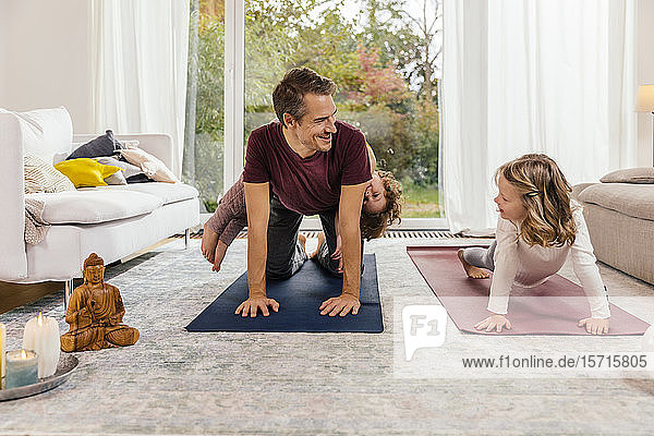 Vater mit Töchtern  die zu Hause im Wohnzimmer Yoga machen