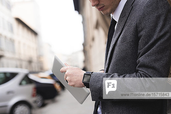 Scherenschnittansicht eines jungen Geschäftsmannes mit digitalem Tablet  der auf eine Smartwatch schaut