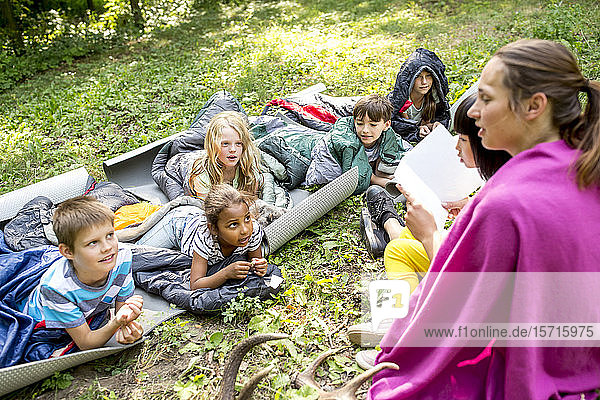Lehrer liest Schulkindern eine Geschichte vor  Camping im Wald