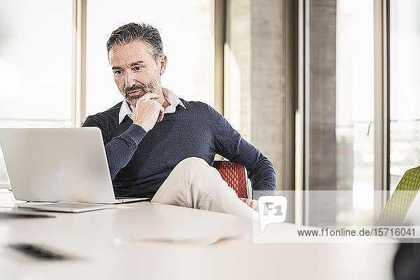 Mature businessman sitting at desk in office using laptop