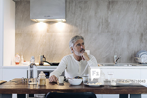 Mature man sitting at table in kitchen at home