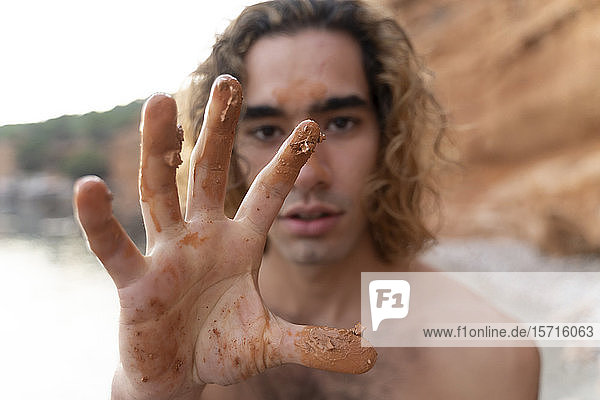 Young man showing his hand with mud on a beach