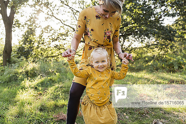 Porträt eines kleinen blonden Mädchens Hand in Hand mit ihrer Mutter auf einer Wiese