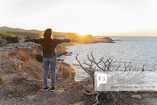 Rothaarige junge Frau steht bei Sonnenuntergang an der Küste  Ibiza  Spanien