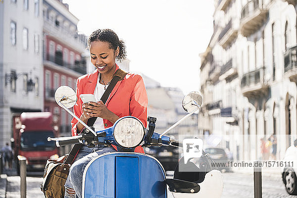 Lächelnde junge Frau benutzt Handy auf Motorroller in der Stadt  Lissabon  Portugal