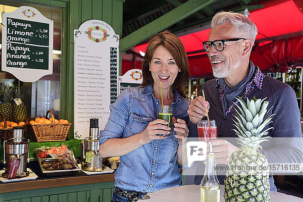 Portrait of happy mature couple drinking a healthy juice at a market stall
