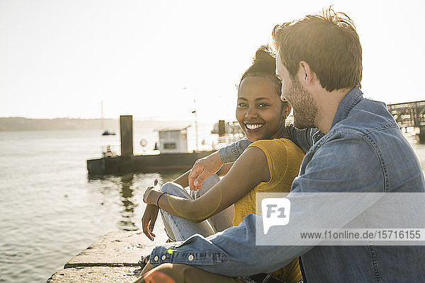 Happy young couple sitting on pier at the waterfront  Lisbon  Portugal