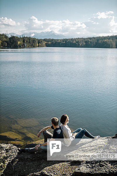 Glückliches Paar sitzt Rücken an Rücken am Seeufer  Forstsee  Kärnten  Österreich