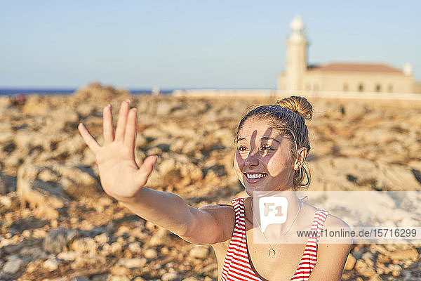 Junge Frau an einem felsigen Strand  das Gesicht mit der Hand abschirmend  Menorca  Spanien