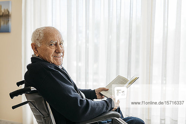 Portrait of smiling senior man sitting in wheelchair with a book