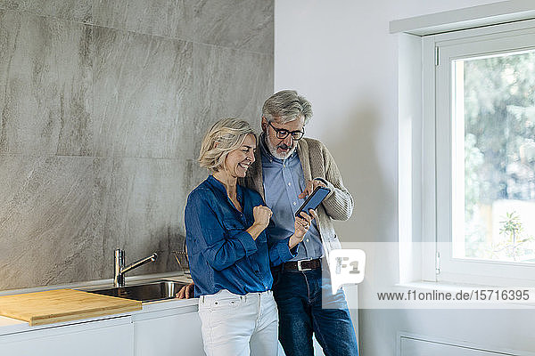 Ein erwachsenes Paar  das zu Hause in der Küche gemeinsam ein Mobiltelefon benutzt