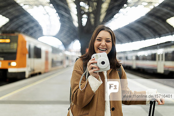 Glückliche junge Frau mit Kamera am Bahnhof