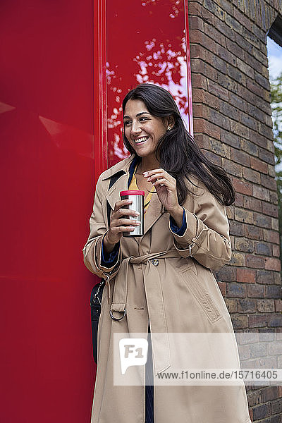 Junge Geschäftsfrau mit wiederverwendbarer Kaffeetasse  an die Wand gelehnt