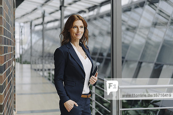 Selbstbewusste Geschäftsfrau hält ein Tablett in einem modernen Bürogebäude