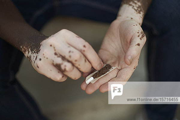 Nahaufnahme eines jungen Mannes mit Vitiligo beim Drehen einer Zigarette