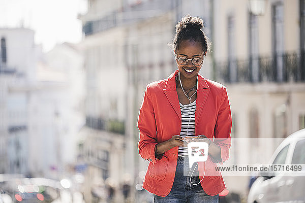 Lächelnde junge Frau mit Kopfhörern mit Smartphone in der Stadt  Lissabon  Portugal