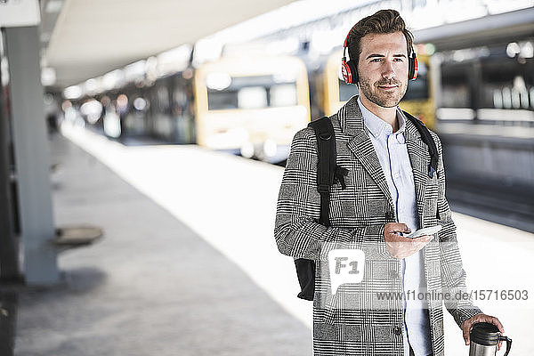 Young businessman with cell phone and headphones at the train station
