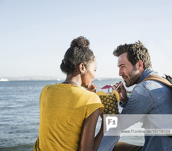 Young couple sitting at the waterfront sharing a drink in a pineapple  Lisbon  Portugal