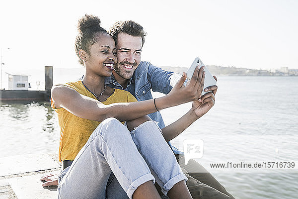Glückliches junges Paar sitzt auf dem Pier am Wasser und macht einen Egoisten  Lissabon  Portugal