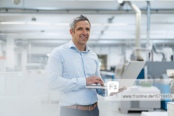Smiling businessman using laptop in factory