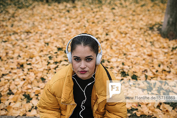 Porträt einer jungen Frau  die im Herbst mit Kopfhörern Musik hört
