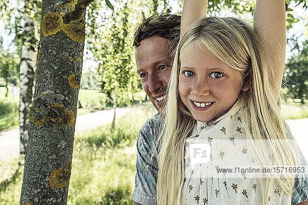 Porträt eines lächelnden Mädchens mit Vater am Ast einer Birke hängend