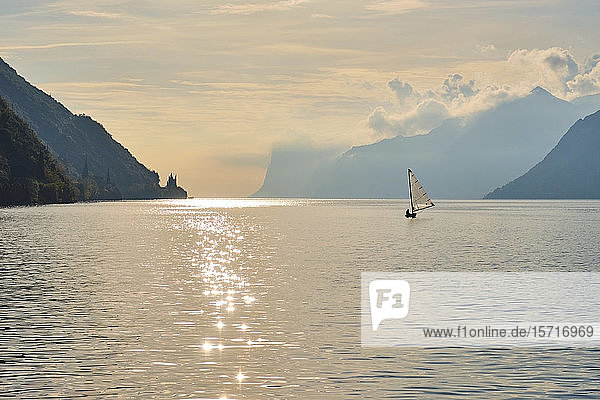 Italy  Trentino  Nago-Torbole  Silhouette of sailboat sailing near coastal cliffs of Lake Garda at moody dawn
