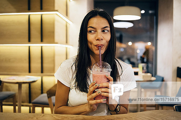 Schwarzhaarige Frau trinkt einen Smoothie im Café