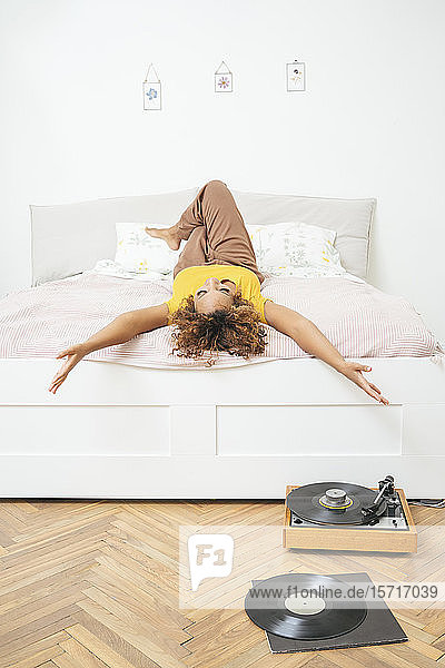 Junge Frau liegt zu Hause im Bett mit Plattenspieler auf dem Boden