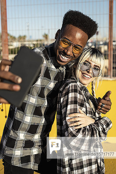 Porträt eines lachenden jungen Paares  das mit einem Smartphone Selbsthilfe betreibt