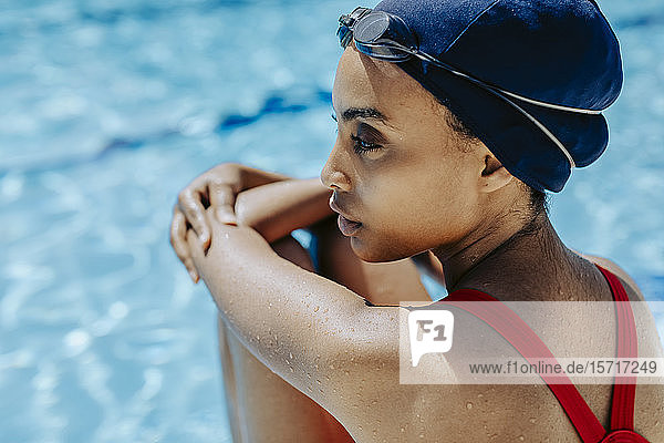 Junge Frau mit Badekappe und Schwimmbrille entspannt sich nach dem Schwimmen am Pool
