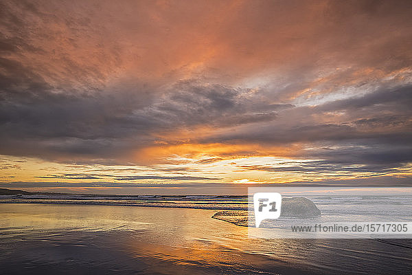 Neuseeland  Tongaporutu  Bewölkter Himmel über sandigem Küstenstrand in der orangefarbenen Dämmerung